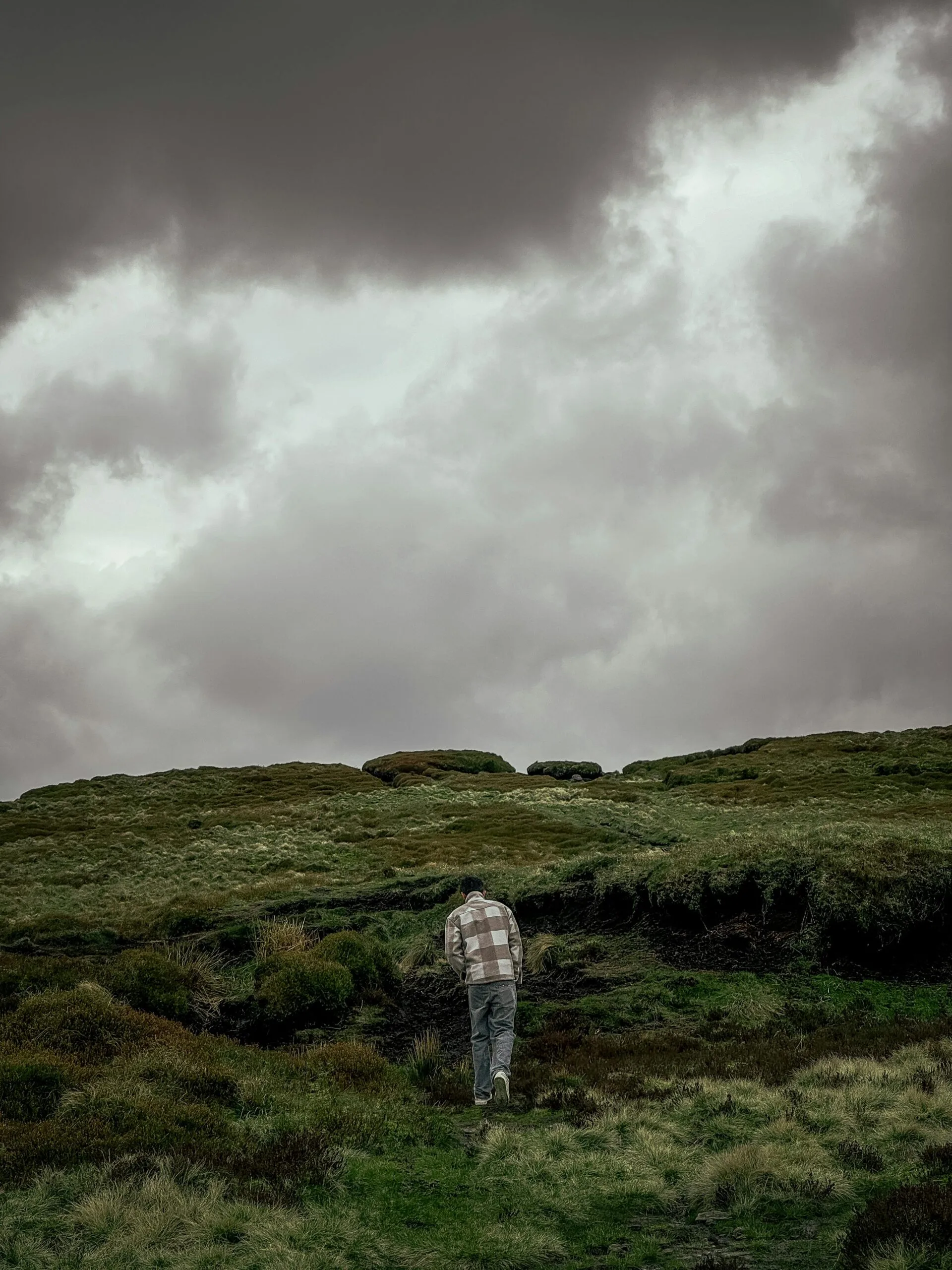 A man walking alone up a moorland path under a heavy grey sky